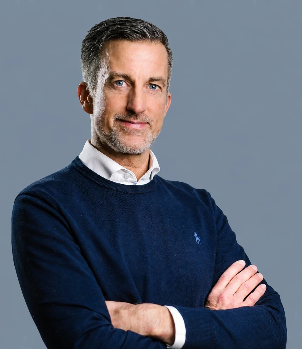 Porträt von Oliver Kober mit verschränkten Armen vor grauem Hintergrund – professionell, souverän und nahbar